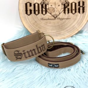 Handgefertigtes Hundehalsband mit beige Gurtband und dunkelbrauner Stickerei des Namens &lsquo;Simba&rsquo;, inklusive passender Leine. Pr&auml;sentiert auf mintfarbenem Kunstfell mit Coorox-Holzlogo im Hintergrund.&ldquo;